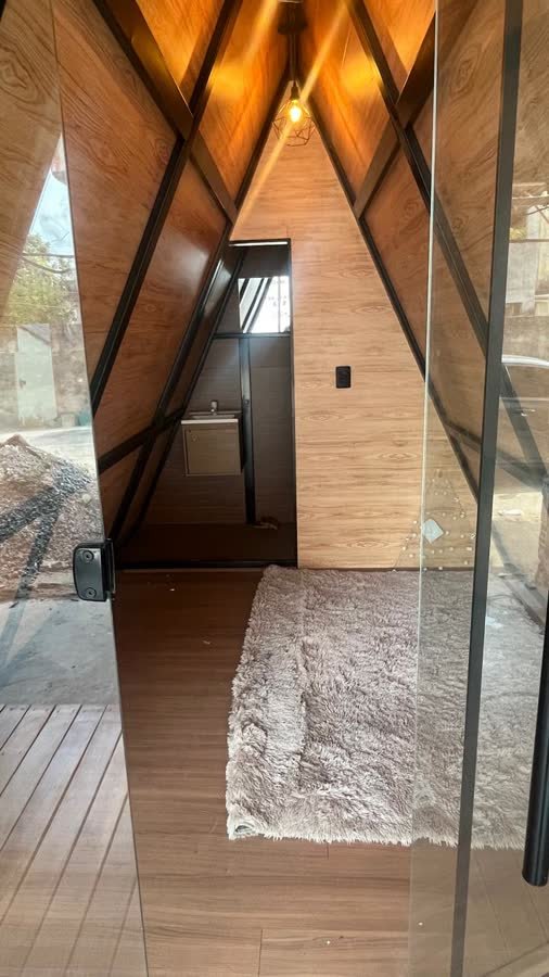 Interior do chalé visto da porta, com forro amadeirado, tapete e a porta do banheiro ao fundo